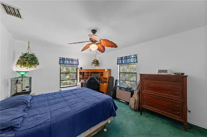 Bright interior space featuring a ceiling fan with light fixture, multiple windows, built-in shelving, and green carpet flooring