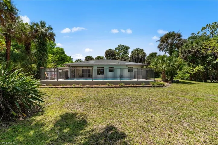 Expansive green space featuring a fenced swimming pool, surrounding patio, and mature tropical landscaping