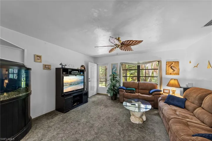 Living area featuring a ceiling fan with leaf-inspired blades, a large bay window, and light-toned walls