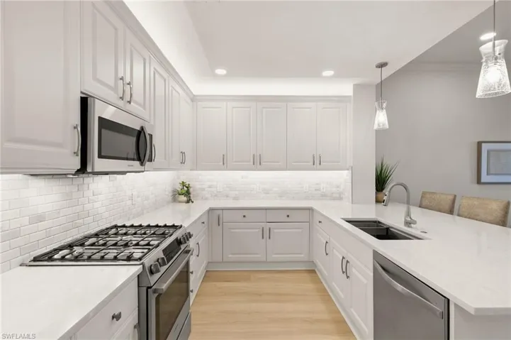 Kitchen with a peninsula, stainless steel appliances, a kitchen bar, white cabinetry, and light stone counters