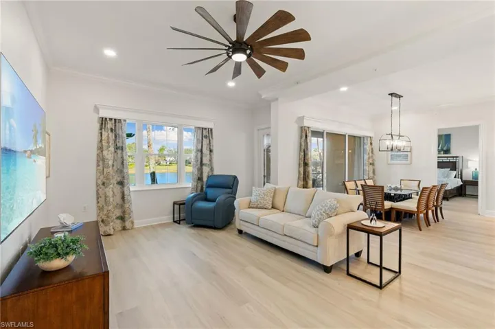 Living room with ornamental molding, light wood-type flooring, hanging lights, and ceiling fan
