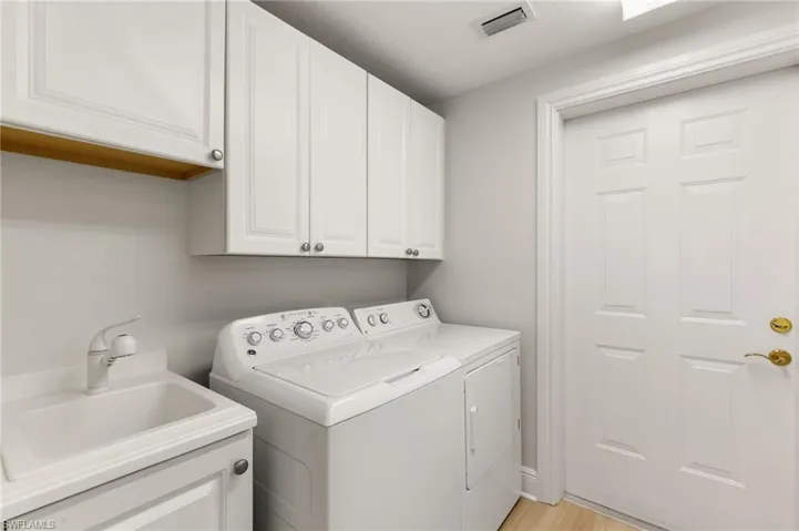 Laundry area featuring washing machine and dryer, cabinet space, and light wood-style floors