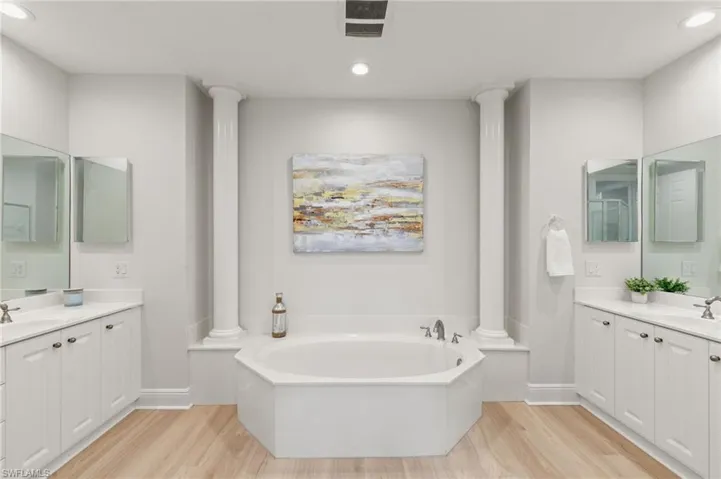 Bathroom featuring light wood-style flooring, ornate columns, two vanities, recessed lighting, and a bath