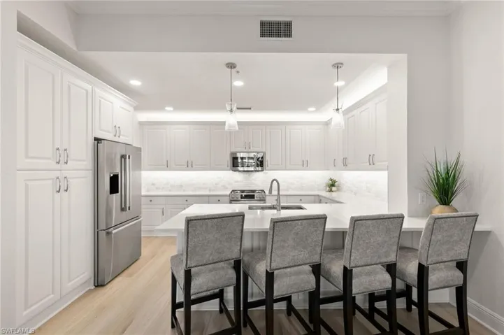 Kitchen featuring a peninsula, white cabinetry, stainless steel appliances, a breakfast bar area, and light wood-style flooring
