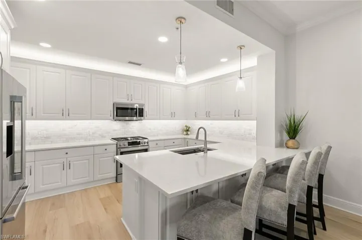 Kitchen with white cabinets, stainless steel appliances, a peninsula, hanging light fixtures, and light wood-type flooring