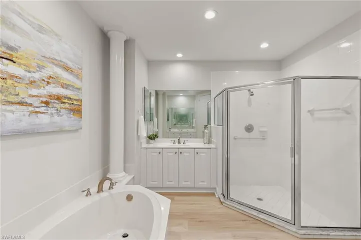 Bathroom featuring light wood-style floors, ornate columns, a garden tub, a stall shower, and vanity