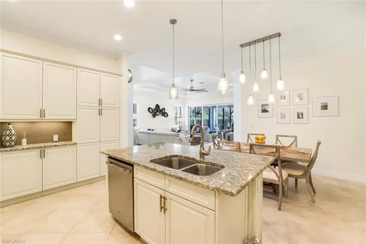 Kitchen with stainless steel dishwasher, ceiling fan, sink, decorative light fixtures, and an island with sink