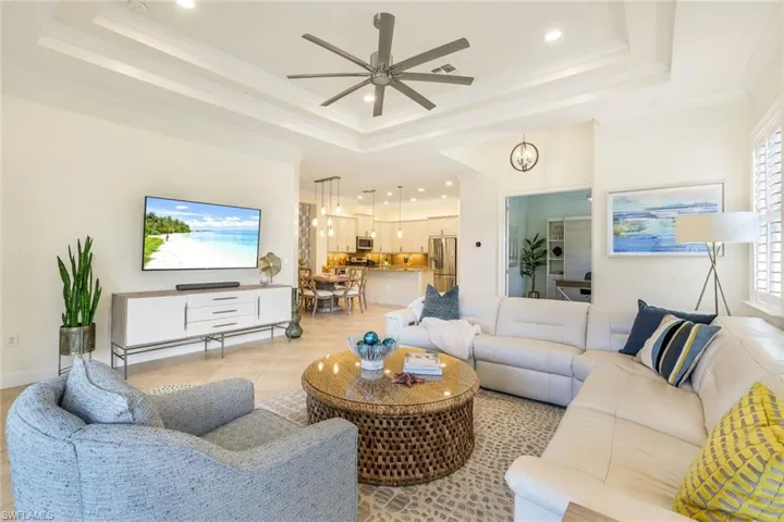 Living room with ceiling fan, a raised ceiling, light tile patterned floors, and crown molding
