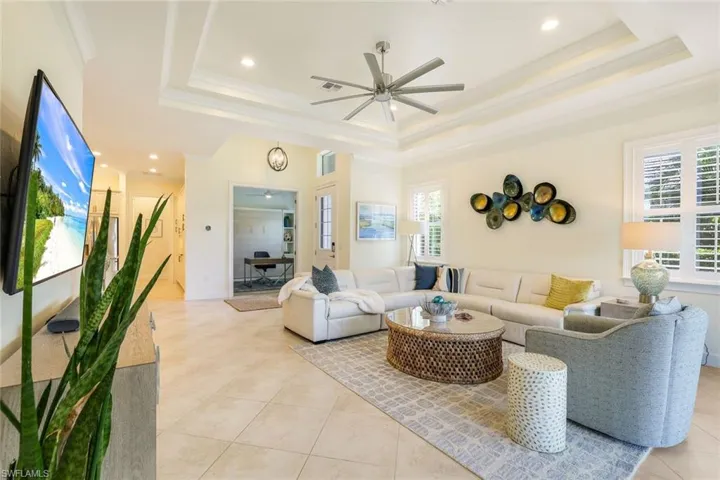 Living room with ceiling fan, a raised ceiling, ornamental molding, and a wealth of natural light