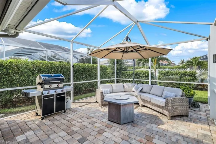 View of patio featuring glass enclosure, an outdoor living space with a fire pit, and a grill
