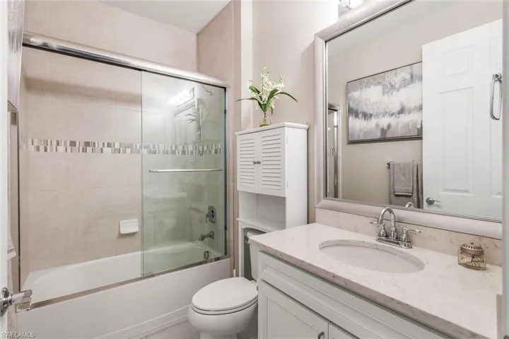 Full bathroom with enclosed tub / shower combo, vanity, and toilet