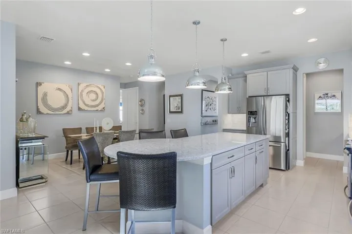 Kitchen featuring a kitchen island, stainless steel fridge, light tile patterned flooring, and a kitchen bar