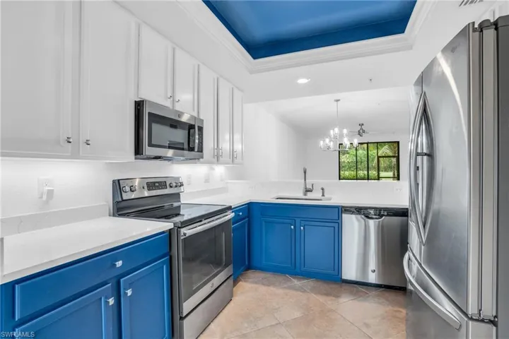 Kitchen featuring appliances with stainless steel finishes, sink, light tile patterned floors, blue cabinets, and a tray ceiling