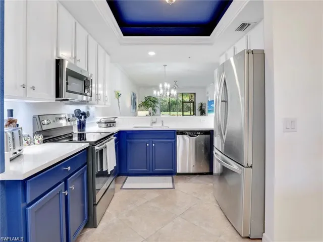 Kitchen featuring stainless steel appliances, an inviting chandelier, light tile patterned floors, blue cabinets, and a tray ceiling