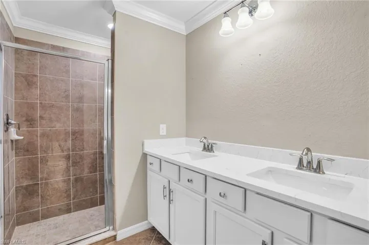 Bathroom with double vanity, an enclosed shower, and crown molding