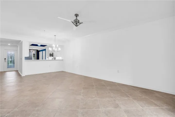 Unfurnished living room featuring light tile patterned flooring, crown molding, and ceiling fan with notable chandelier