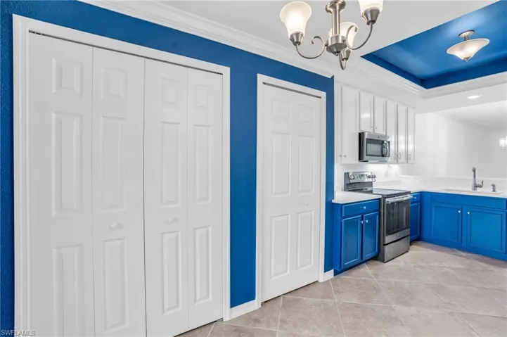 Kitchen with light tile patterned flooring, blue cabinets, stainless steel appliances, ornamental molding, and sink