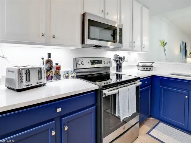 Kitchen featuring appliances with stainless steel finishes, light stone countertops, light tile patterned flooring, blue cabinets, and ornamental molding