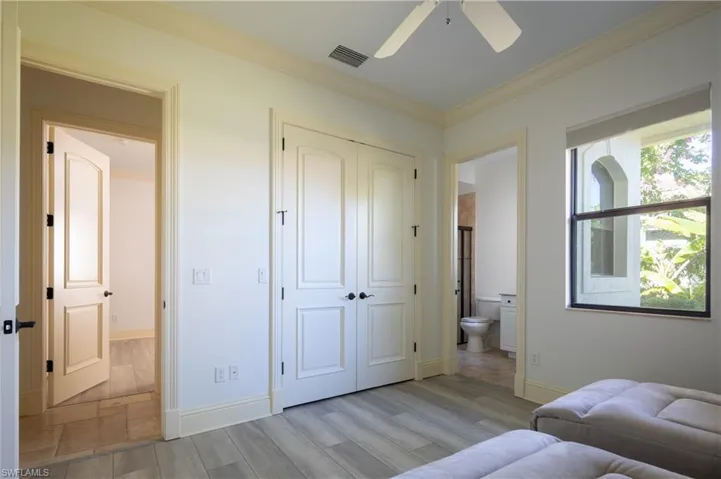 Bedroom with wood finish floors, crown molding, a closet, ensuite bath, and a ceiling fan