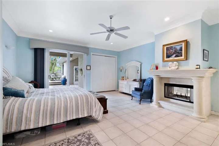 Bedroom with light tile patterned flooring, crown molding, a multi sided fireplace, and ceiling fan