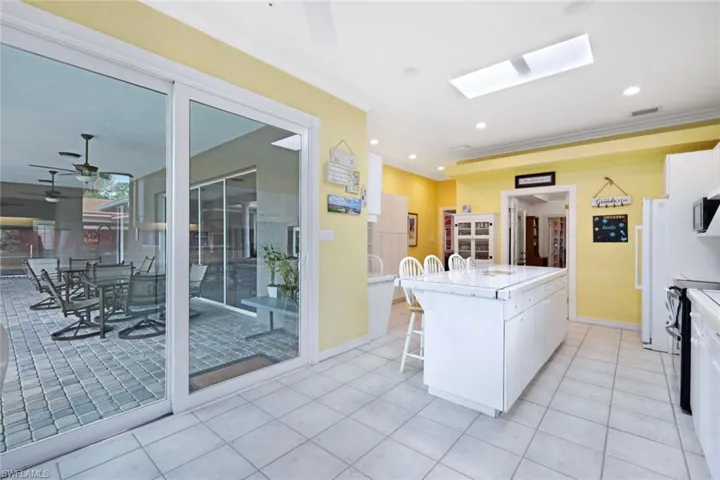 Kitchen featuring white cabinets, light tile patterned floors, a kitchen island, a skylight, and ceiling fan