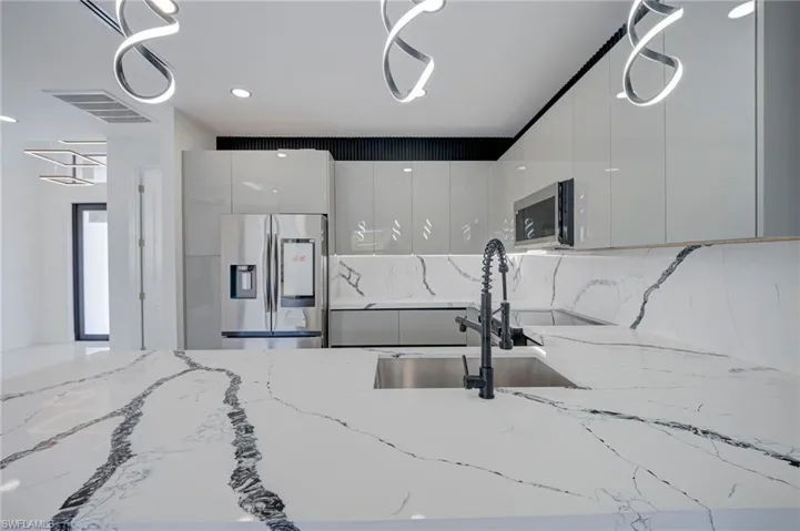 Kitchen featuring modern cabinets, stainless steel appliances, light stone countertops, and tasteful backsplash