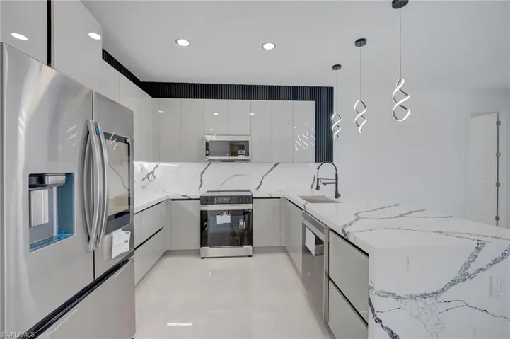 Kitchen with stainless steel appliances, a peninsula, light stone countertops, decorative light fixtures, and modern cabinets