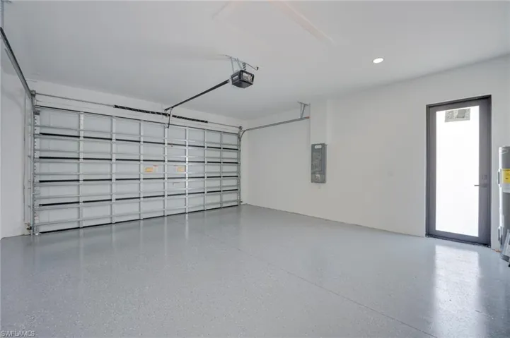 Garage with recessed lighting, electric panel, water heater, and a garage door opener
