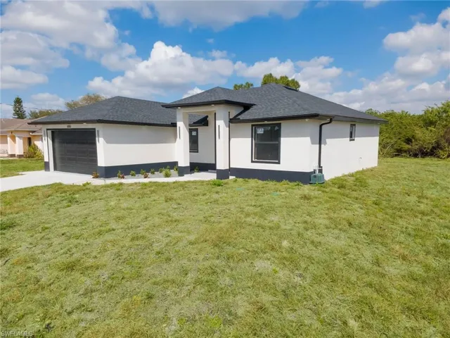 Prairie-style home with stucco siding, a front lawn, an attached garage, driveway, and roof with shingles