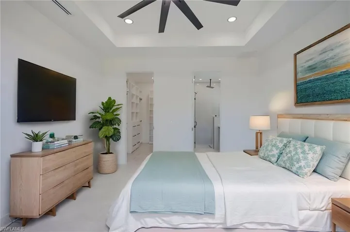 Bedroom with a tray ceiling, a ceiling fan, ensuite bath, and recessed lighting