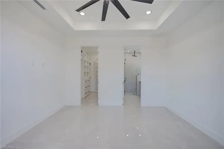 Unfurnished bedroom with a tray ceiling, a walk in closet, recessed lighting, and ceiling fan