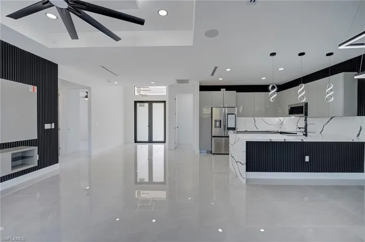 Kitchen featuring modern cabinets, light stone counters, stainless steel appliances, decorative light fixtures, and a ceiling fan