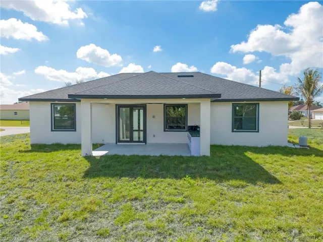 Back of house with stucco siding, a lawn, a shingled roof, and a patio