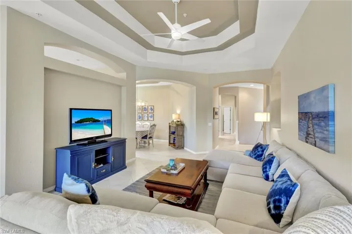 Recessed tray ceiling with ceiling fan, tile flooring, and arched wall openings