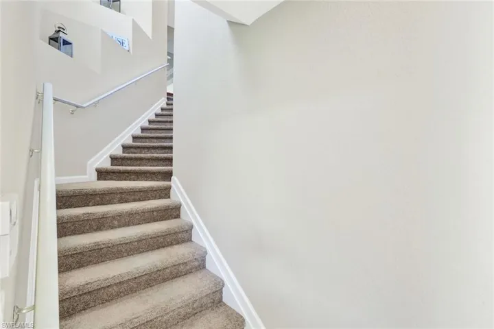 Carpeted staircase with white risers and a contrasting gray handrail