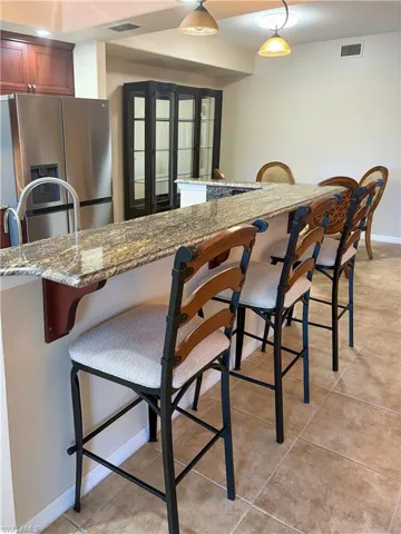 Kitchen with stainless steel fridge with ice dispenser, dark stone countertops, a breakfast bar, pendant lighting, and light tile patterned floors
