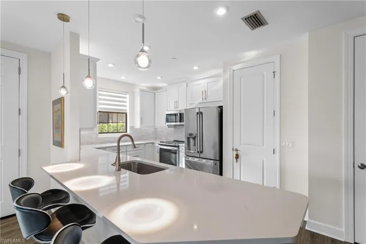 Kitchen with decorative light fixtures, stainless steel appliances, a peninsula, white cabinets, and a breakfast bar area