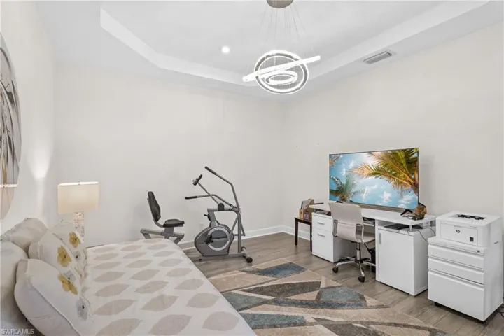 Bedroom with a tray ceiling, light wood-style flooring, a desk, and recessed lighting