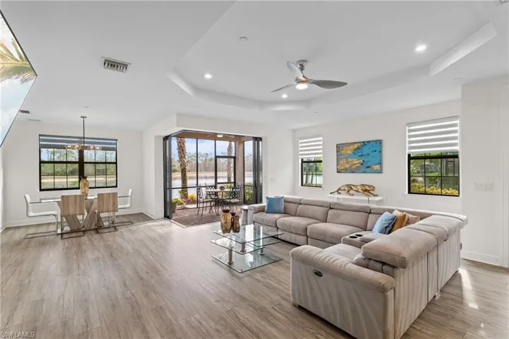 Living room featuring recessed lighting, light wood-style floors, a ceiling fan, a chandelier, and a tray ceiling