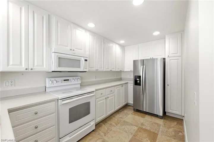 Kitchen with white appliances, white cabinetry, light countertops, recessed lighting, and stone finish floors