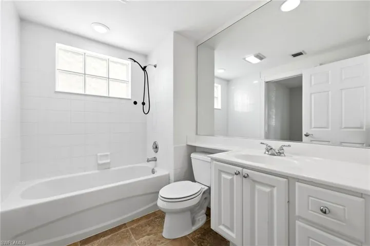 Full bath featuring vanity, bathtub / shower combination, healthy amount of natural light, and dark tile patterned floors
