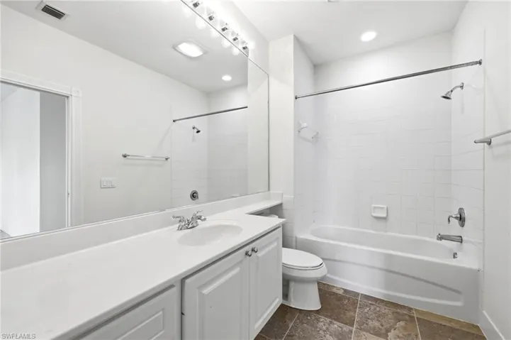 Full bath with vanity, dark stone finish flooring, and  shower combination