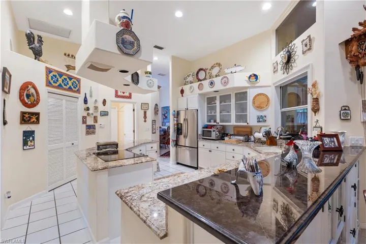 Kitchen with light stone countertops, stainless steel fridge, a kitchen island, and light tile floors