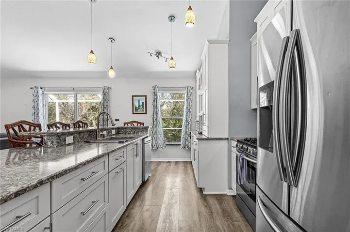 Kitchen with stainless steel appliances, quartz countertops, dark wood-style flooring, and hanging light fixtures