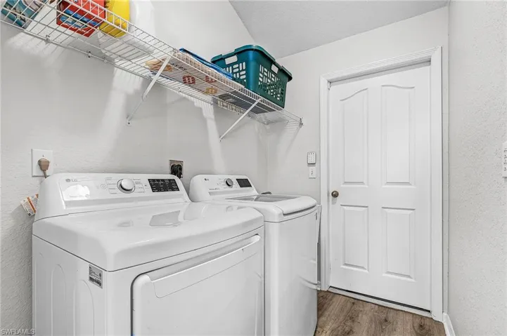Laundry room with a textured wall, washing machine and clothes dryer, and wood finished floors