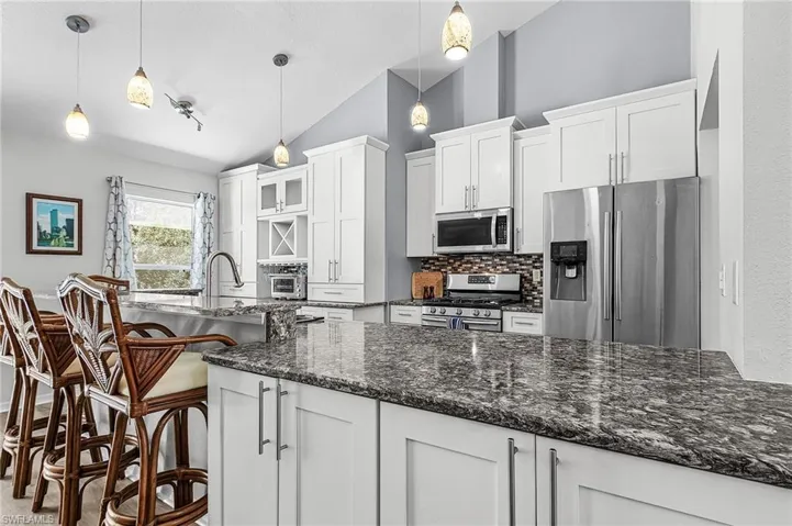 Kitchen with stainless steel appliances, white cabinets, quartz counters, backsplash, and lofted ceiling