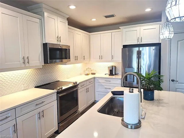 Kitchen featuring stainless steel appliances, white cabinets, decorative backsplash, light stone counters, and pendant lighting