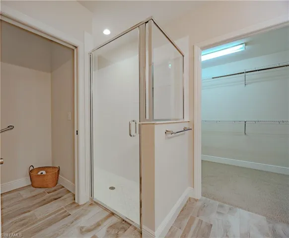 Full bathroom with a spacious closet, a stall shower, and light colored carpet