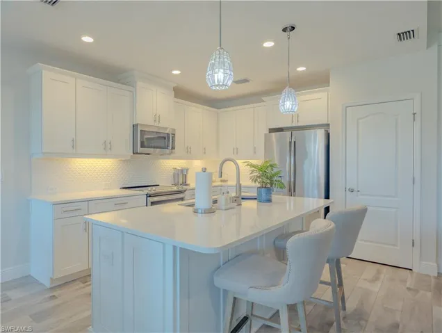 Kitchen with white cabinetry, a breakfast bar area, stainless steel appliances, decorative light fixtures, and light wood-style flooring