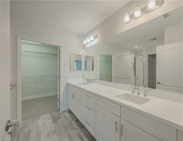 Full bathroom featuring a shower stall, a spacious closet, double vanity, and light wood-type flooring